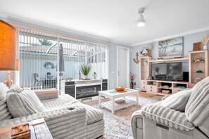 A living room with a fireplace, a TV, and a large window with blinds. - Bonita 3BR | Pool + Tennis | Monthly Min (Bonita Springs)