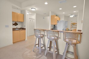 A modern kitchen with wooden cabinets, a central island with bar stools, and a refrigerator. - Fort Myers | Resort Pool + Spa | 2BR (Fort Myers)