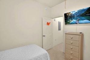 Une chambre à coucher comprenant un lit, une commode, une porte ornée d’un élément décoratif et un téléviseur fixé au mur qui diffuse une vue panoramique.