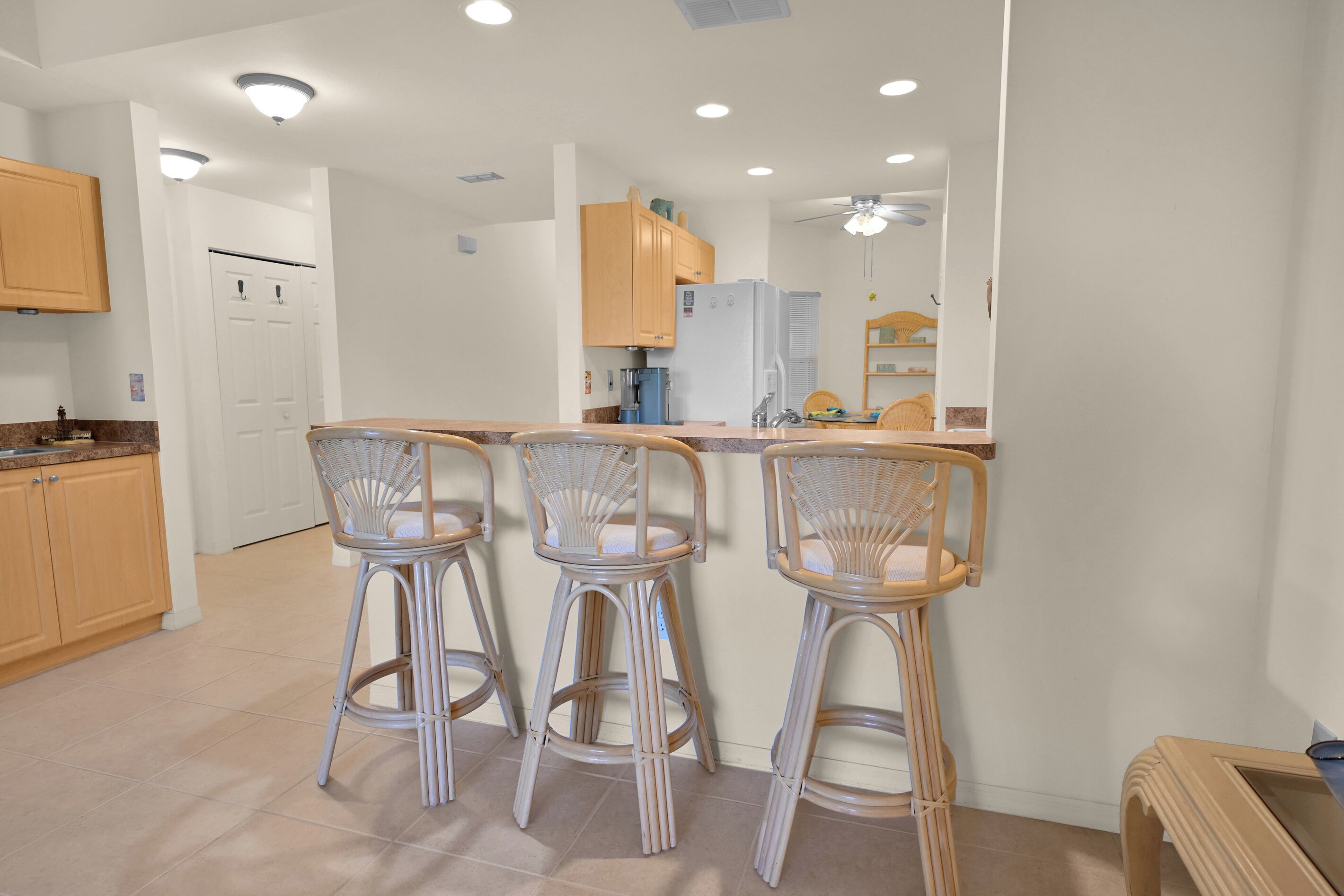 A kitchen with three bar stools, a refrigerator, and a coffee machine.