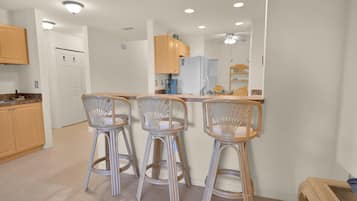 A kitchen with three bar stools, a refrigerator, and a coffee machine.