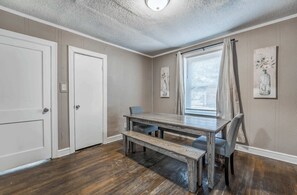 Comedor con mesa de madera y bancos, una ventana con persianas y dos puertas.