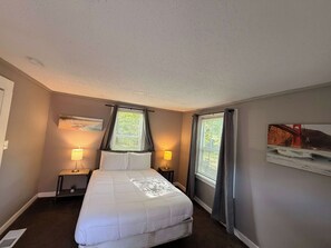 Una habitación de hotel con una cama, dos mesitas de noche con lámparas, una ventana con cortinas y un cuadro en la pared.