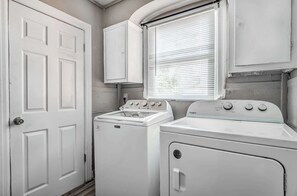 A laundry room with a front-loading washer and dryer, a window with blinds, and white cabinetry.