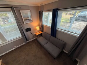 Ein Zimmer mit einer grauen Couch, einem kleinen Tisch mit einer Lampe und einem Bild an der Wand.