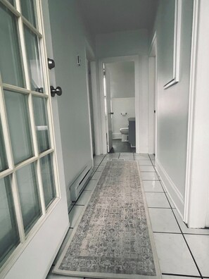Un couloir avec un tapis à motifs, des murs blancs et une porte donnant sur une salle de bain.