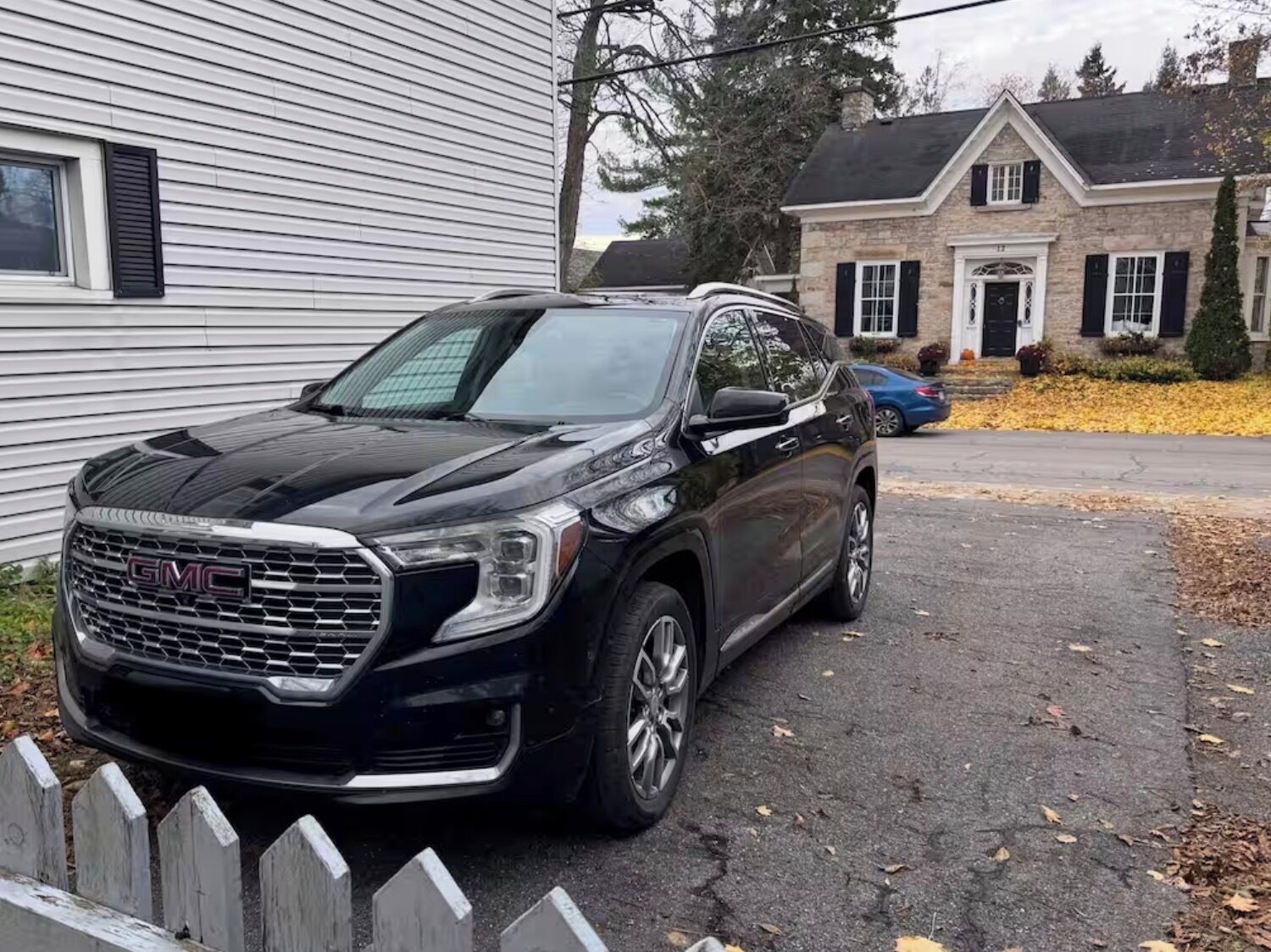 A black GMC SUV parked in front of a house with a stone facade and a white exterior.