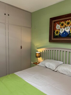 A bedroom with a bed, a nightstand, a lamp, a wardrobe, and a painting on the wall. - The Mexican Casita (Cancun)
