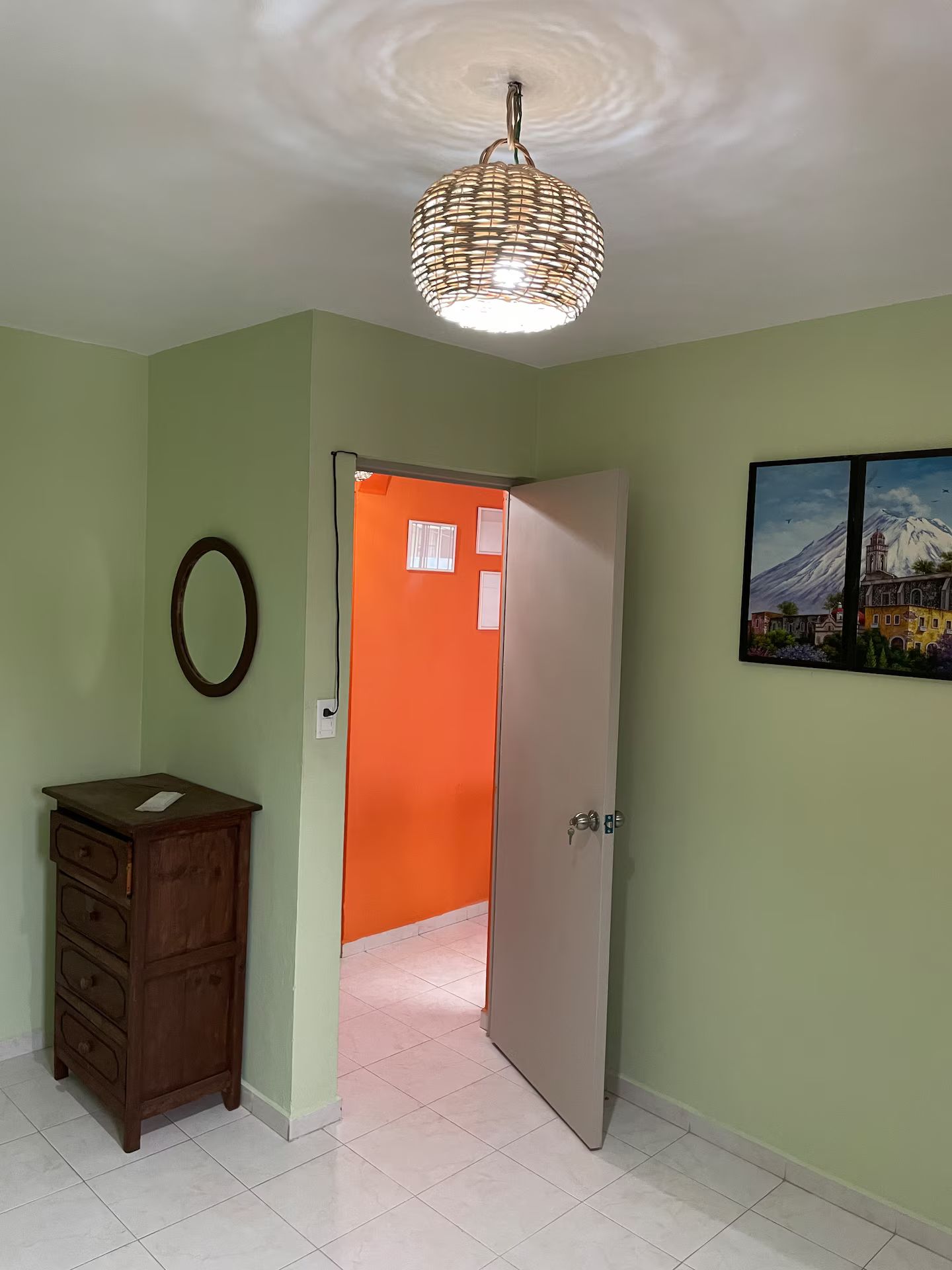 Een kamer met een houten dressoir, een deur naar een oranje kamer en een aan de muur hangend schilderij.
