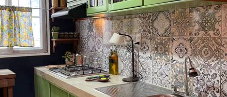A kitchen with green cabinets, a tiled backsplash, and a window with curtains.