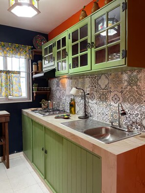 Een keuken met groene kastjes, een betegelde achterwand en een raam met gordijnen.