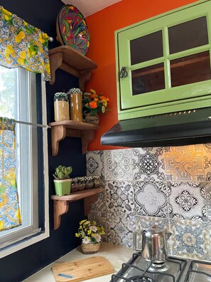 A kitchen with a stove, a window with a curtain, and shelves with jars and flowers. - The Mexican Casita (Cancun)
