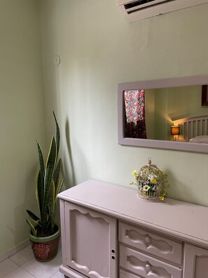 A room with a potted plant, a dresser with drawers, a mirror, and a window with a colorful view. - The Mexican Casita (Cancun)