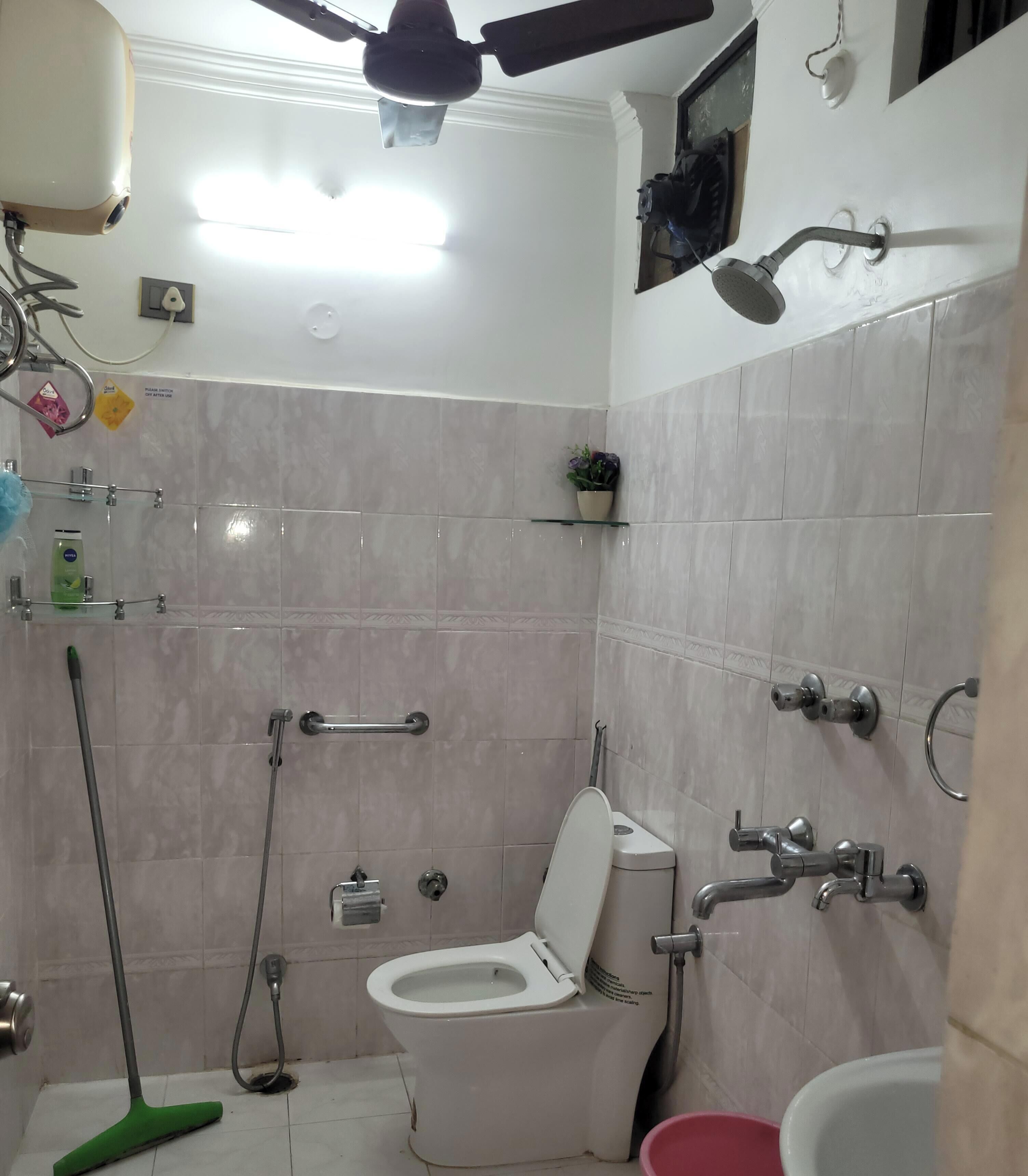 Et badeværelse med toilet, bidet, bruser og loftventilator.