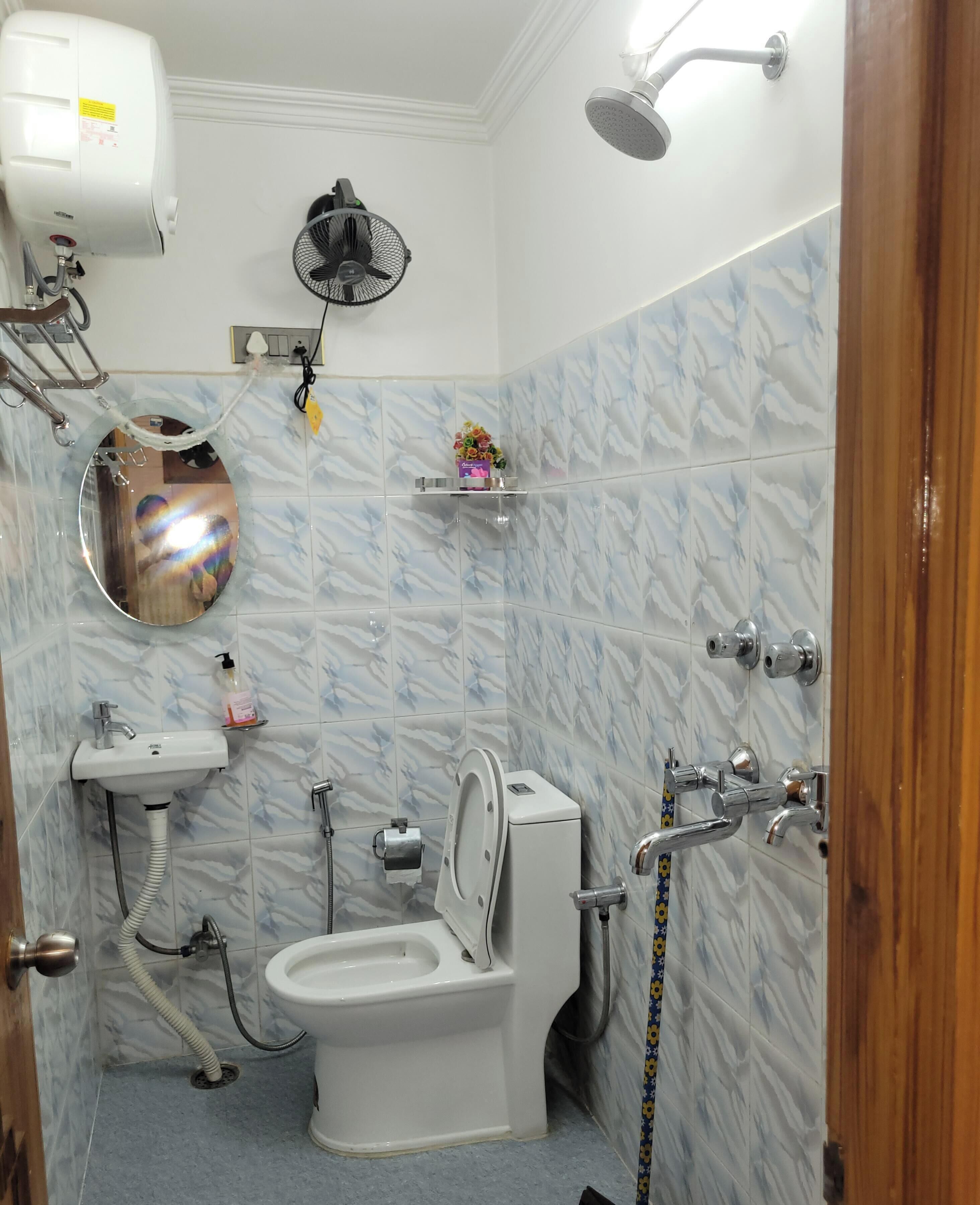 Et badeværelse med toilet, håndvask, brusebad og ventilator.