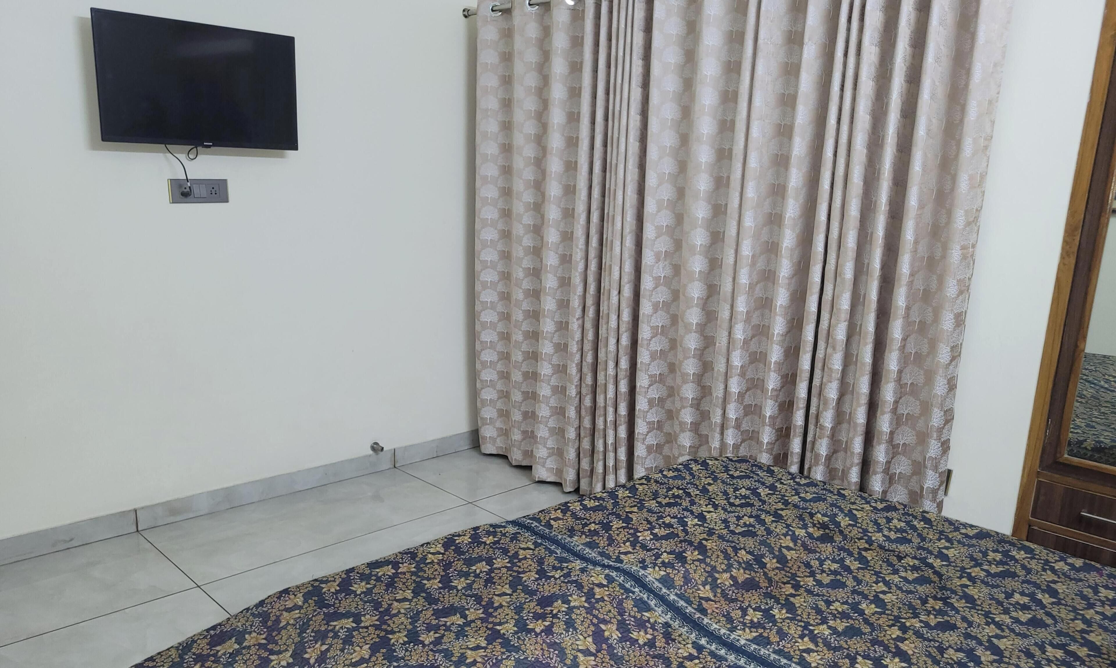 Een kamer met een bed, een aan de muur bevestigde televisie en een gordijn met een boommotief.