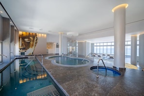 A modern indoor swimming pool with a large mural, large windows, and a spacious layout.