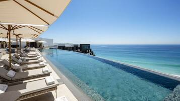 A poolside area with lounge chairs and umbrellas, overlooking a clear blue ocean.
