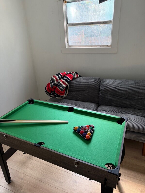 A pool table with balls and cues, a green felt surface, and a sofa with a striped blanket.