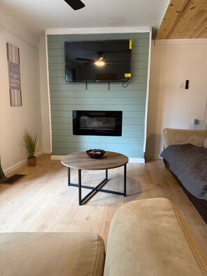 A living room with a flat-screen TV mounted on a green wall, a round coffee table, a sofa, and a fireplace.