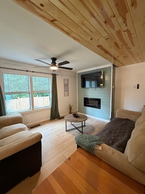 A living room with a ceiling fan, a fireplace, and a TV mounted on the wall. - Peaceful Private Cabin near Everything Breakfast Hot Tub Firepit Fenced Backyard (Pigeon Forge)