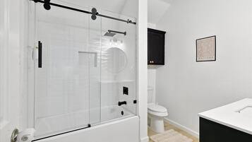 Un baño moderno con cabina de ducha de vidrio, inodoro blanco y mueble negro.