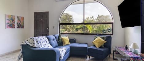 Un salón con un sofá modular, una mesa de centro y un ventanal con vistas a la vegetación.