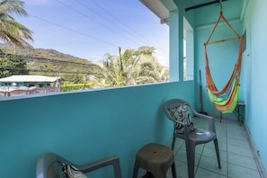 Ein Balkon mit einer Hängematte, zwei Stühlen und Blick auf einen Hügel mit Vegetation.