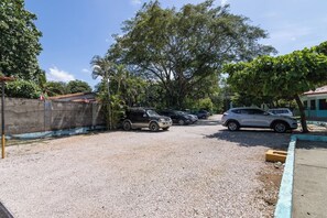 A gravel parking area with several cars parked, surrounded by trees and a fence.