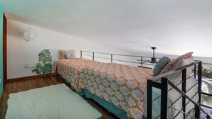 A bedroom with a bed, a white rug, a ceiling fan, and a view of the ocean.