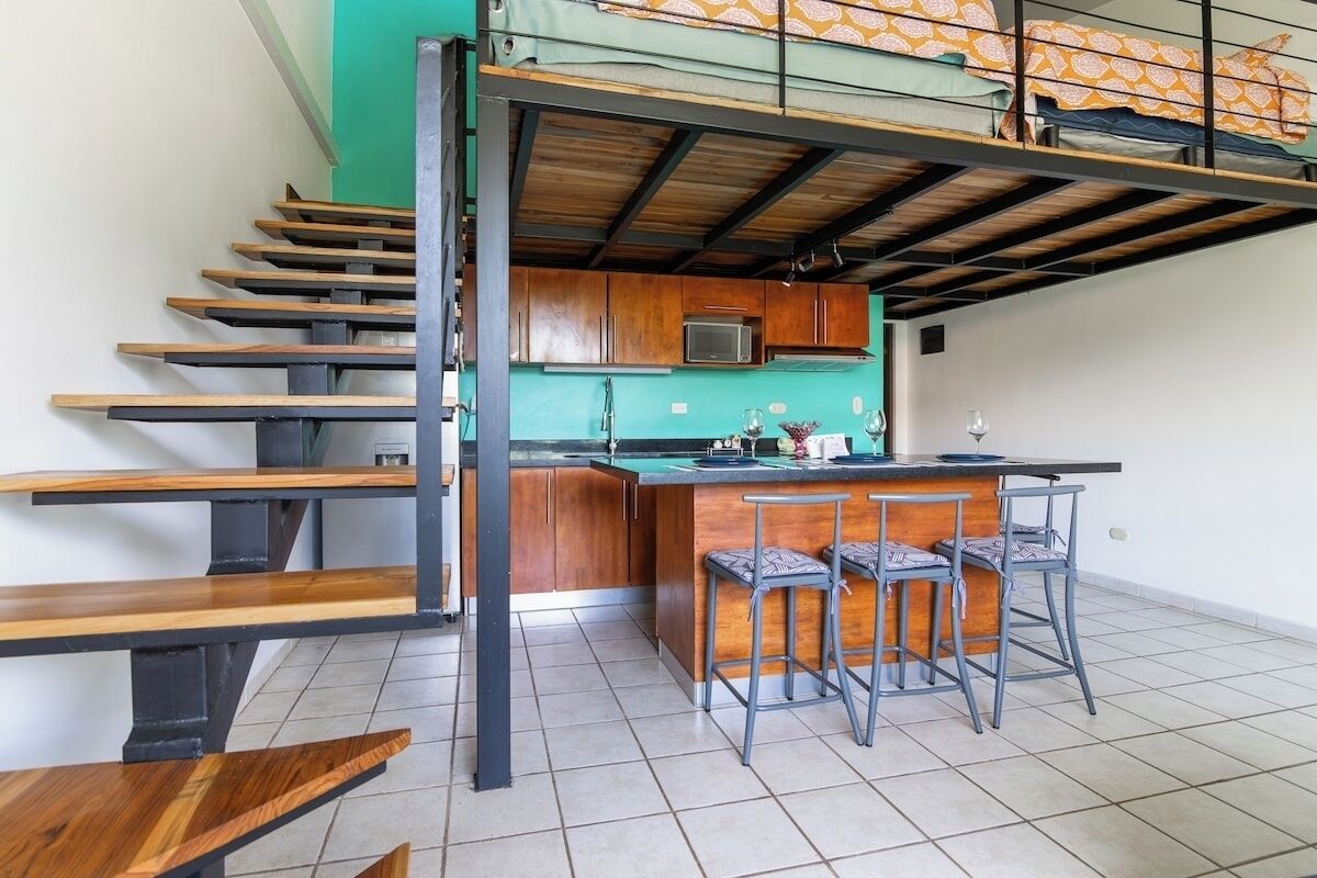 A compact kitchen with a central island, bar stools, and a staircase with wooden steps.