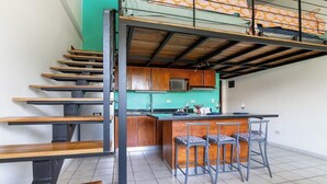 A compact kitchen with a central island, bar stools, and a staircase with wooden steps.