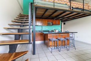 A compact kitchen with a central island, bar stools, and a staircase with wooden steps.
