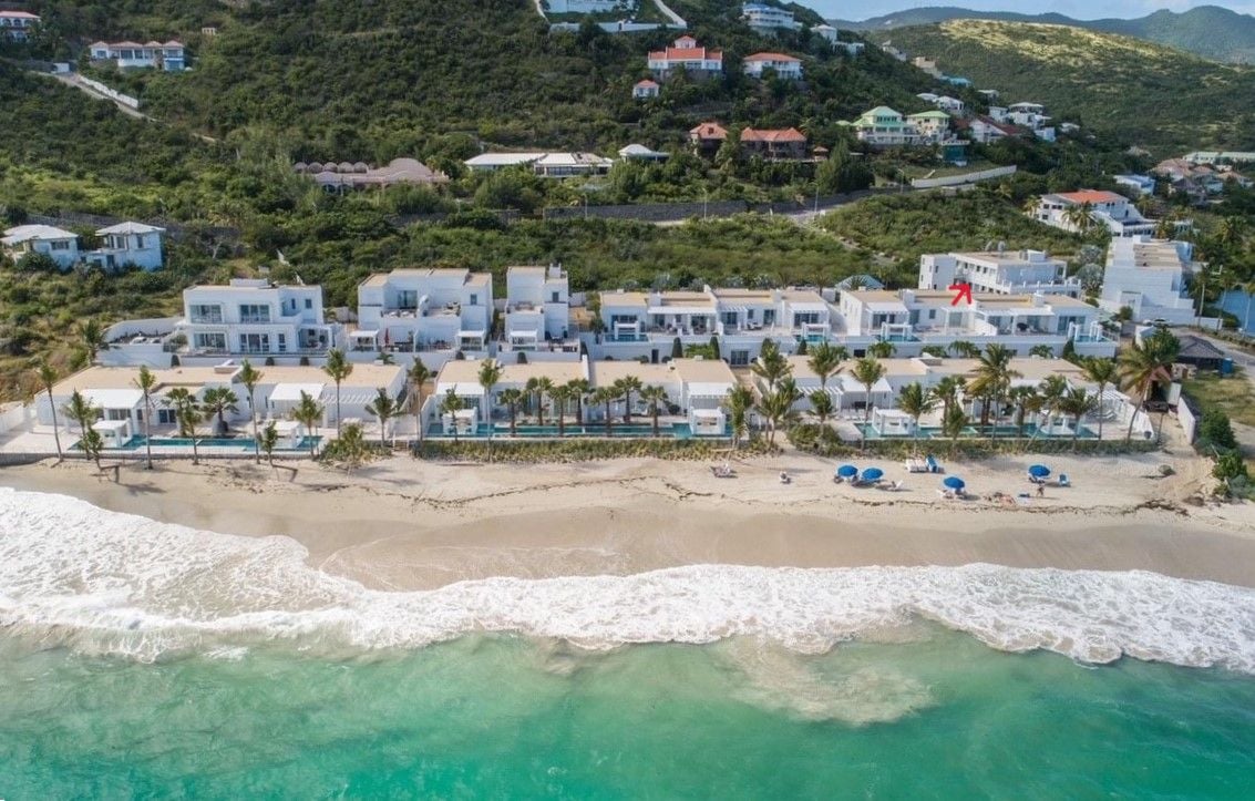 A coastal resort with beachfront villas, palm trees, and a sandy beach.