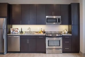 A modern kitchen with dark cabinets, stainless steel appliances, and a granite countertop. - Harbor free indoor parking (Baltimore)