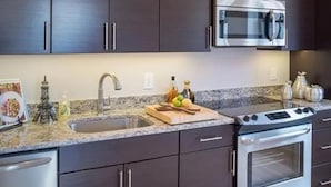 Une cuisine avec des meubles de couleur sombre, un four à micro-ondes en acier inoxydable, une cuisinière et un plan de travail en granit.