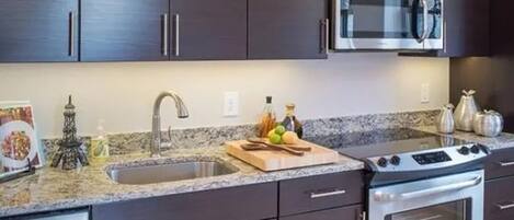 A kitchen with dark cabinets, a stainless steel microwave, a stove, and a granite countertop.