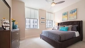 Une chambre à coucher comprenant un lit, une commode, un ventilateur de plafond et de grandes fenêtres.