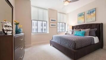 A bedroom with a bed, dresser, ceiling fan, and large windows.