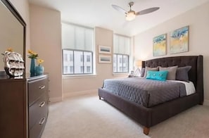 A bedroom with a bed, dresser, ceiling fan, and large windows. - Harbor free indoor parking (Baltimore)