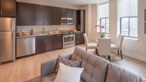 Une cuisine moderne avec des meubles de couleur sombre, des appareils en acier inoxydable et un coin repas comprenant une table et des chaises blanches.