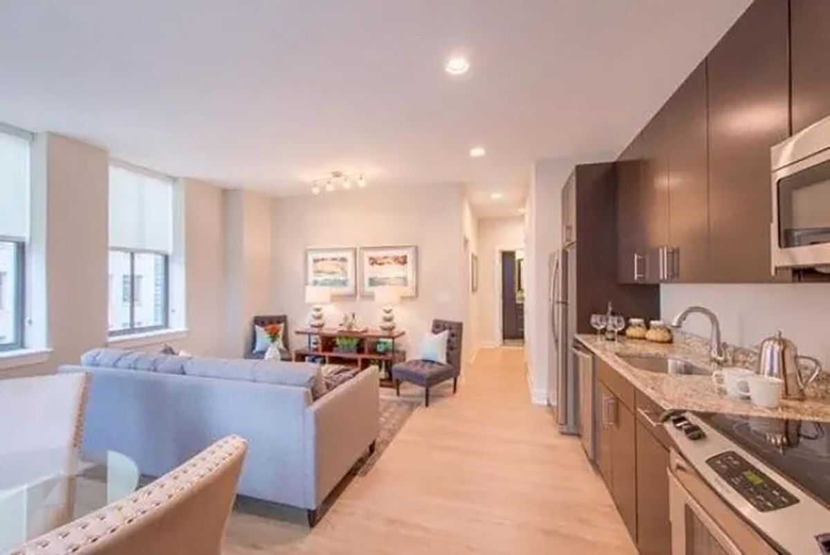 A modern kitchen with dark cabinets, stainless steel appliances, and a dining area with a sofa and table.