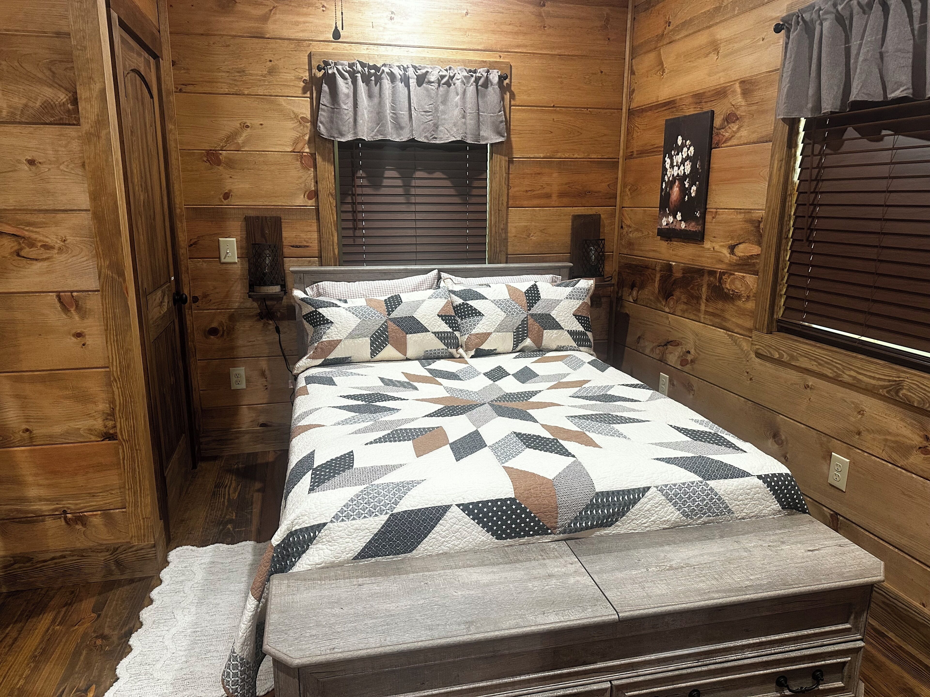 Un dormitorio tipo cabaña de madera con una cama, una ventana con persianas, un altavoz montado en la pared y una colcha acolchada.