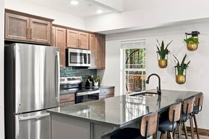 A modern kitchen with stainless steel appliances, wooden cabinets, and a central island with bar stools. - Luxury 4BR Cabin, Hot Tub, 5 Min to Big Cedar! (Hollister)