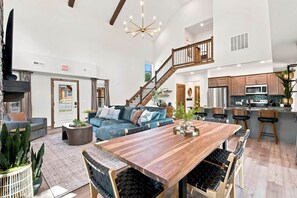 A spacious living area with a large wooden dining table, comfortable seating, a staircase, and a modern kitchen with stainless steel appliances. - Luxury 4BR Cabin, Hot Tub, 5 Min to Big Cedar! (Hollister)