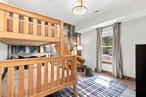 A room with a bunk bed, a lamp, a window with curtains, and a view of the outdoors. - Luxury 4BR Cabin, Hot Tub, 5 Min to Big Cedar! (Hollister)