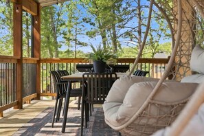 Un patio exterior con una terraza de madera, una mesa con sillas, un sillón colgante y una planta en maceta.