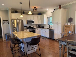 A kitchen with white cabinets, stainless steel appliances, a granite countertop, and bar stools.