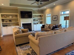 A living room with a fireplace, a television, and a ceiling fan.