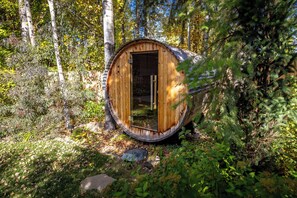 A wooden barrel structure with a door, surrounded by trees and foliage. - Seasonal Retreat | Private Yard w/Sauna & Spa (Whitefish)